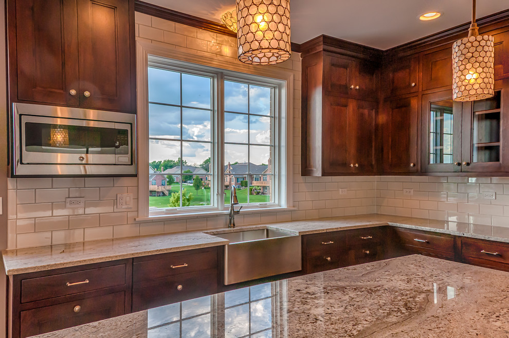 Inspiration for a mid-sized transitional u-shaped dark wood floor eat-in kitchen remodel in Chicago with a farmhouse sink, recessed-panel cabinets, medium tone wood cabinets, granite countertops, white backsplash, ceramic backsplash, stainless steel appliances and an island