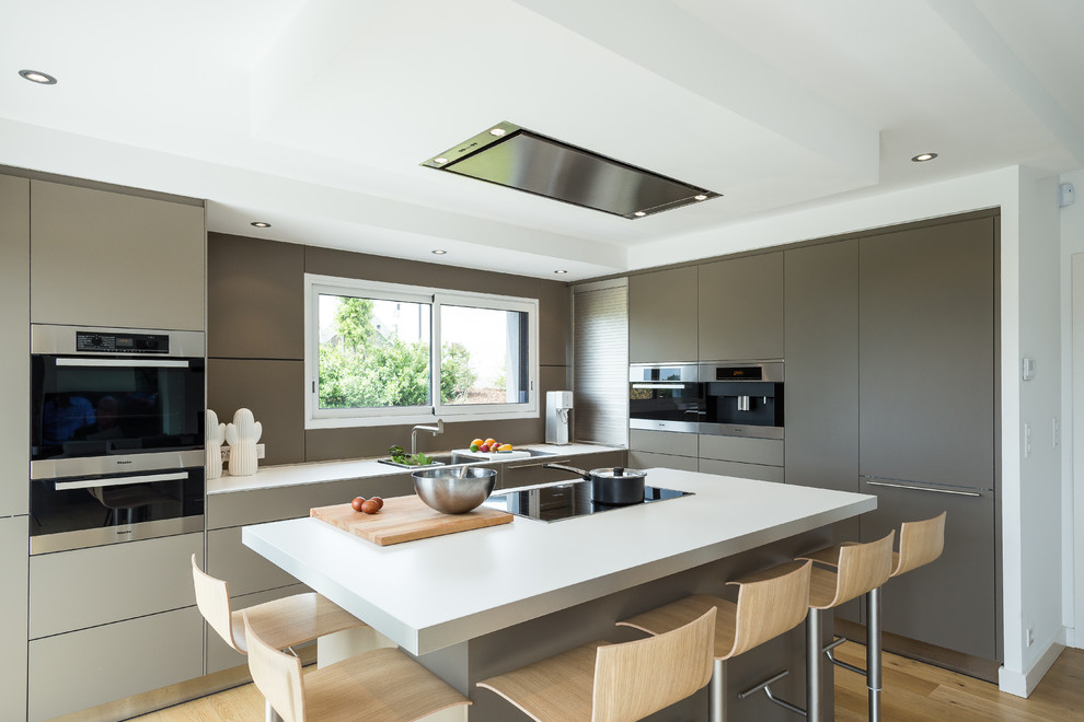 Inspiration for a contemporary l-shaped eat-in kitchen in Brest with an integrated sink, brown cabinets, laminate benchtops, brown splashback, stainless steel appliances, medium hardwood floors, with island, brown floor and white benchtop.