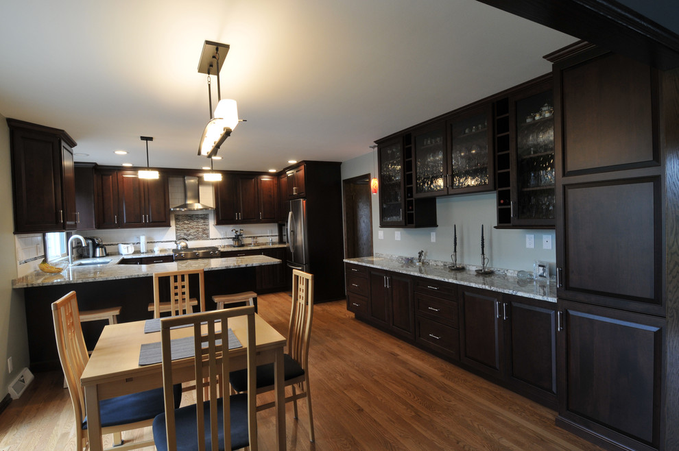 Mid-sized transitional u-shaped medium tone wood floor eat-in kitchen photo in Milwaukee with a double-bowl sink, dark wood cabinets, granite countertops, multicolored backsplash, ceramic backsplash, stainless steel appliances and a peninsula