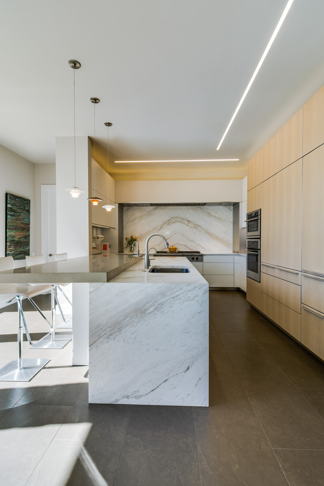Inspiration for a large modern l-shaped eat-in kitchen in Dallas with an undermount sink, flat-panel cabinets, light wood cabinets, marble benchtops, white splashback, stone slab splashback, stainless steel appliances, ceramic floors and a peninsula.
