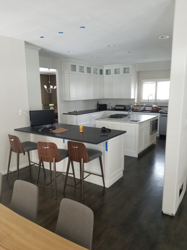 Inspiration for a large transitional u-shaped dark wood floor and brown floor eat-in kitchen remodel in Denver with an undermount sink, shaker cabinets, white cabinets, quartz countertops, stainless steel appliances, an island and black countertops