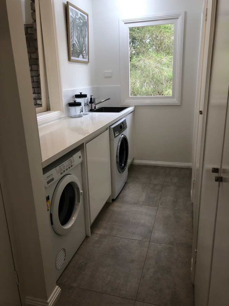 Inspiration for a small contemporary galley dedicated laundry room in Melbourne with a single-bowl sink, white cabinets, quartz benchtops, white splashback, ceramic splashback, white walls, ceramic floors, a side-by-side washer and dryer and beige floor.