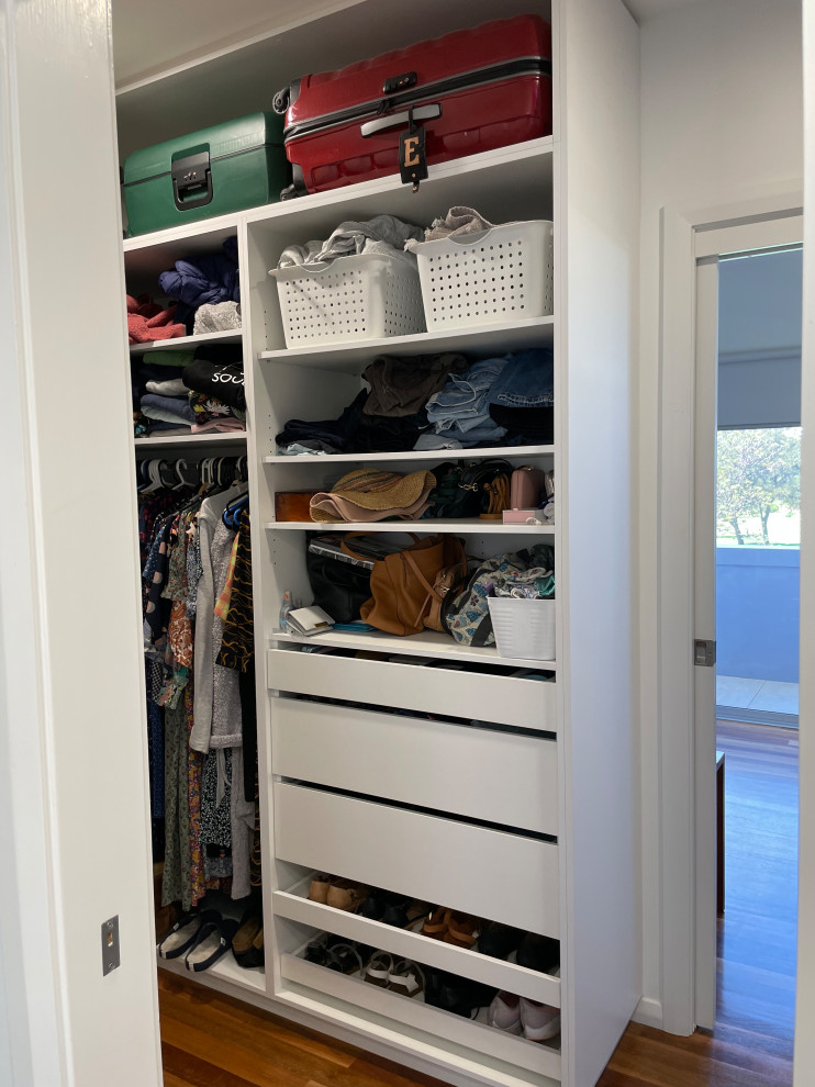 Inspiration for a small contemporary gender-neutral walk-in wardrobe in Wollongong with flat-panel cabinets, white cabinets, light hardwood floors and brown floor.