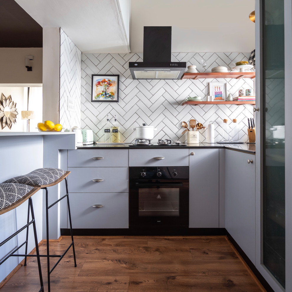 Photo of an eclectic l-shaped kitchen in Chennai with flat-panel cabinets, grey cabinets, white splashback, black appliances, medium hardwood floors, no island, brown floor and black benchtop.