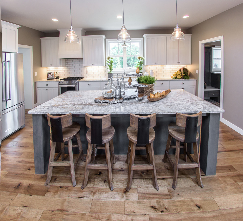 Inspiration for a mid-sized transitional galley light wood floor and brown floor kitchen remodel with a farmhouse sink, shaker cabinets, white cabinets, granite countertops, white backsplash, subway tile backsplash, stainless steel appliances and an island
