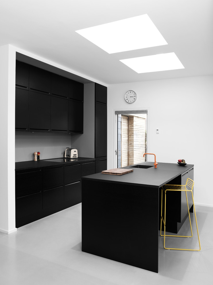 Photo of a mid-sized scandinavian galley separate kitchen in Copenhagen with an integrated sink, flat-panel cabinets, black cabinets, wood benchtops, black appliances, linoleum floors and with island.
