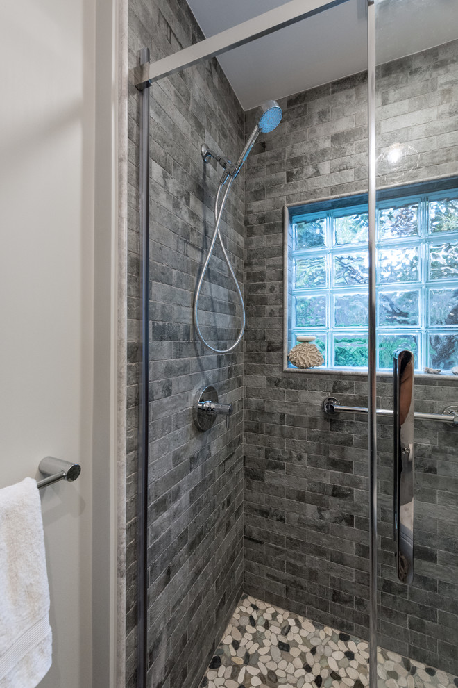 Design ideas for a mid-sized contemporary master bathroom in Providence with flat-panel cabinets, dark wood cabinets, a curbless shower, a two-piece toilet, gray tile, stone tile, grey walls, pebble tile floors, a wall-mount sink, multi-coloured floor, a hinged shower door and white benchtops.