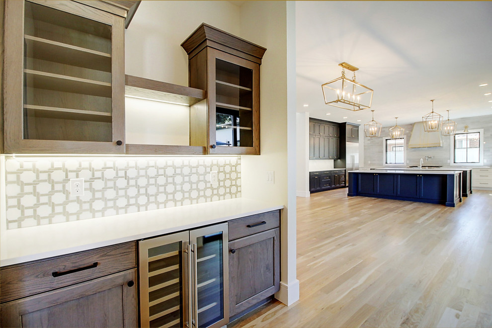 This is an example of a large transitional single-wall home bar in Denver with recessed-panel cabinets, dark wood cabinets, solid surface benchtops, white splashback, ceramic splashback, light hardwood floors, brown floor and white benchtop.