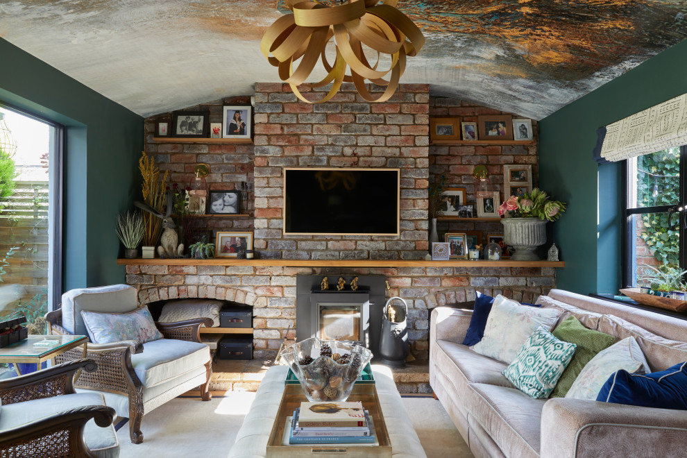 Stilmix Wohnzimmer mit grüner Wandfarbe, Teppichboden, Kamin, Kaminumrandung aus Backstein, TV-Wand, beigem Boden, gewölbter Decke, Tapetendecke und Ziegelwänden in Gloucestershire