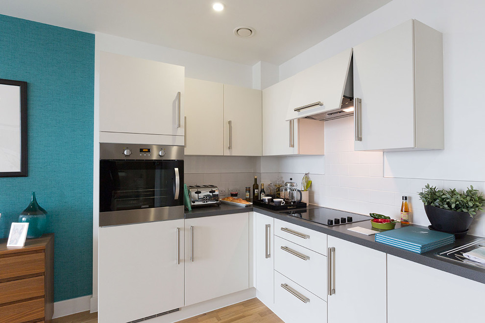 Design ideas for a contemporary l-shaped kitchen in London with a drop-in sink, flat-panel cabinets, white cabinets, white splashback, stainless steel appliances, light hardwood floors and no island.