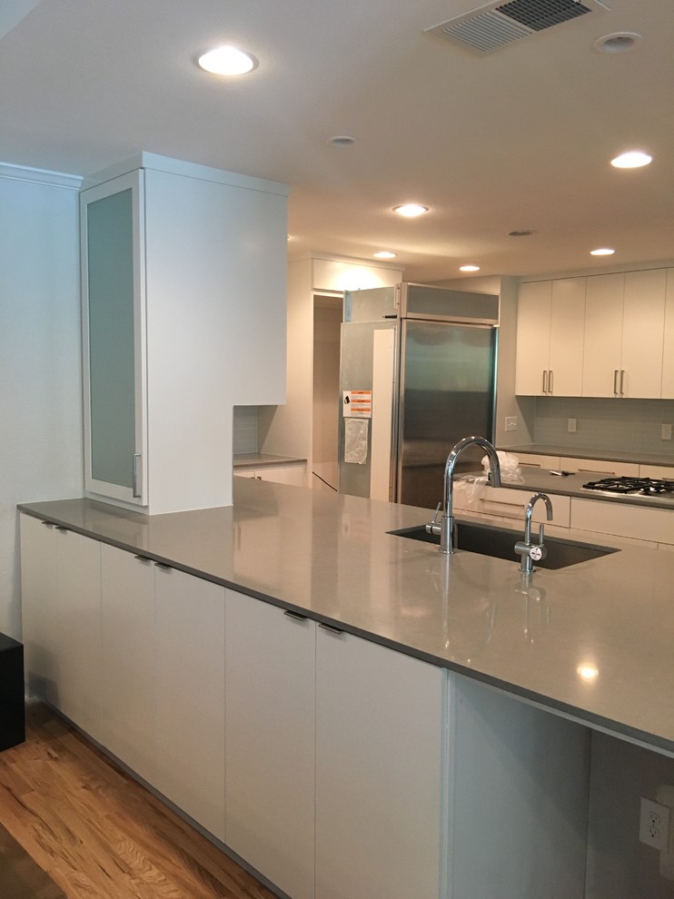 Inspiration for a large transitional u-shaped light wood floor kitchen remodel in Dallas with an undermount sink, flat-panel cabinets, white cabinets, quartz countertops, gray backsplash, glass tile backsplash, stainless steel appliances and an island