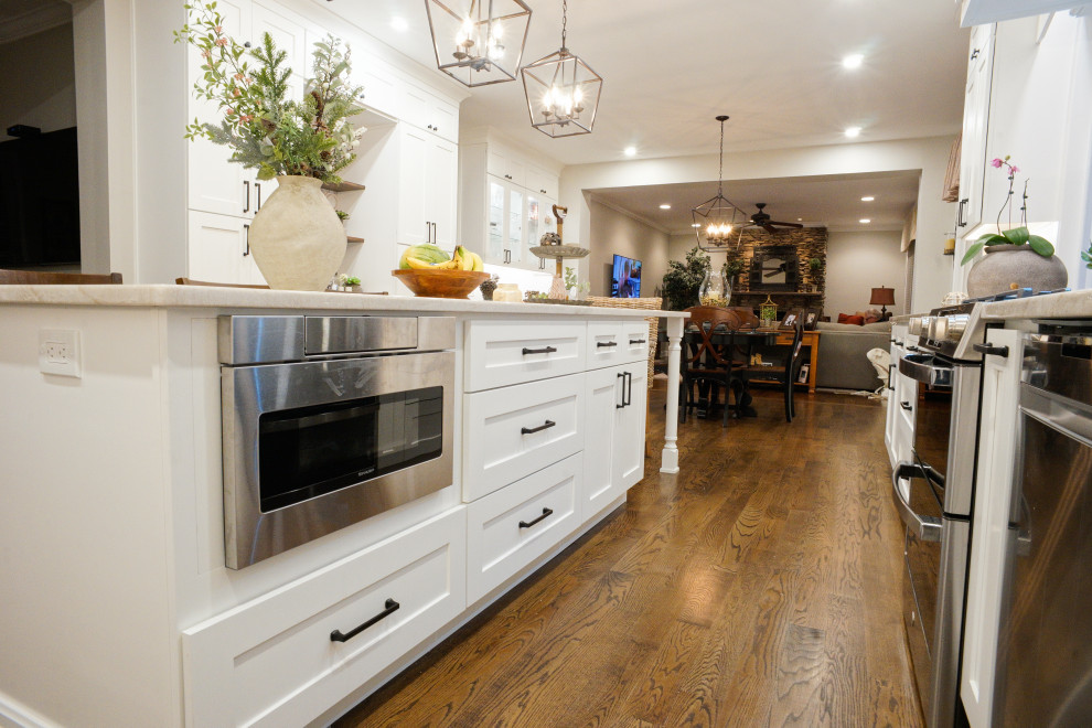 This is an example of a country l-shaped eat-in kitchen in Philadelphia with a farmhouse sink, shaker cabinets, white cabinets, quartzite benchtops, multi-coloured splashback, ceramic splashback, dark hardwood floors, with island and brown floor.