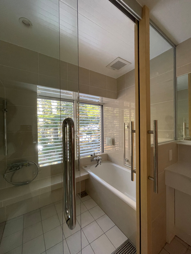 На фото: маленькая главная ванная комната в стиле модернизм с фасадами островного типа, белыми фасадами, накладной ванной, душевой комнатой, унитазом-моноблоком, бежевой плиткой, керамической плиткой, бежевыми стенами, полом из керамогранита, монолитной раковиной, столешницей из искусственного камня, белым полом, душем с раздвижными дверями, белой столешницей, тумбой под одну раковину и встроенной тумбой для на участке и в саду
