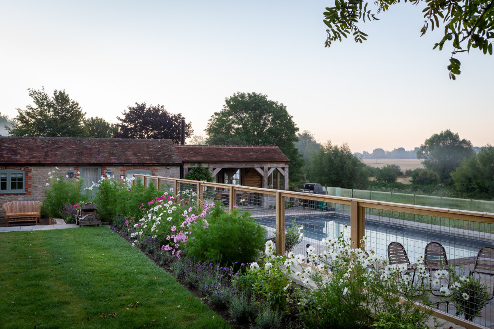 Geometrischer, Großer Landhaus Garten im Sommer, hinter dem Haus mit Blumenbeet, direkter Sonneneinstrahlung, Natursteinplatten und Steinzaun in Oxfordshire