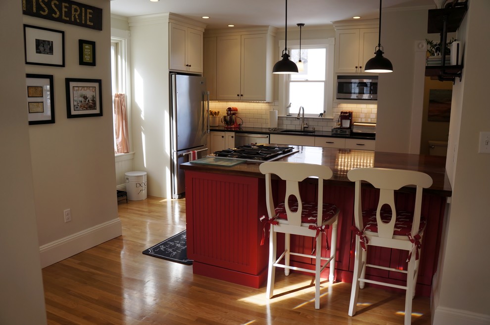Small mountain style l-shaped light wood floor and beige floor enclosed kitchen photo in Boston with an undermount sink, recessed-panel cabinets, granite countertops, white backsplash, subway tile backsplash, stainless steel appliances, an island, white cabinets and black countertops