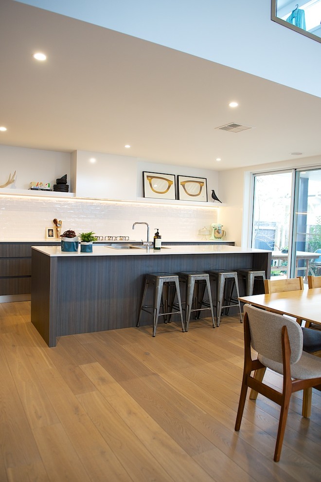 Photo of a contemporary galley kitchen in Sydney with a double-bowl sink, flat-panel cabinets, dark wood cabinets, solid surface benchtops, white splashback, subway tile splashback, stainless steel appliances, medium hardwood floors and with island.
