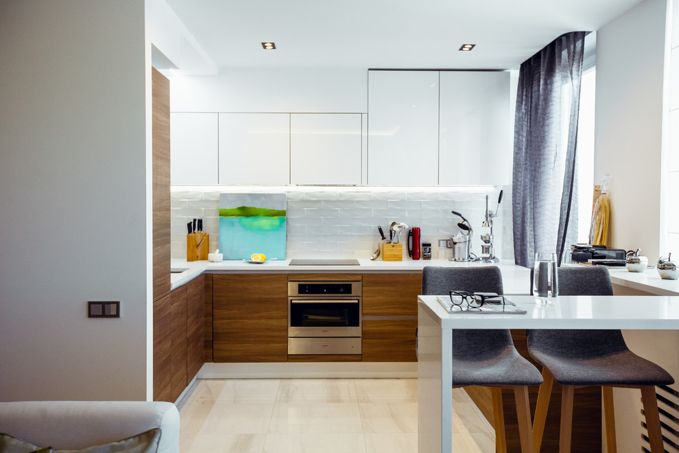 This is an example of a mid-sized contemporary l-shaped open plan kitchen in Saint Petersburg with flat-panel cabinets, medium wood cabinets, white splashback, ceramic splashback, panelled appliances, no island, beige floor and white benchtop.