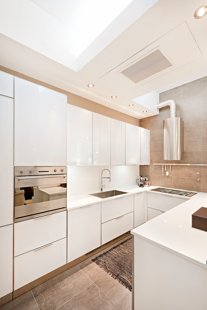 Inspiration for a mid-sized contemporary u-shaped kitchen in Other with a drop-in sink, flat-panel cabinets, white cabinets, solid surface benchtops, white splashback, stainless steel appliances and porcelain splashback.