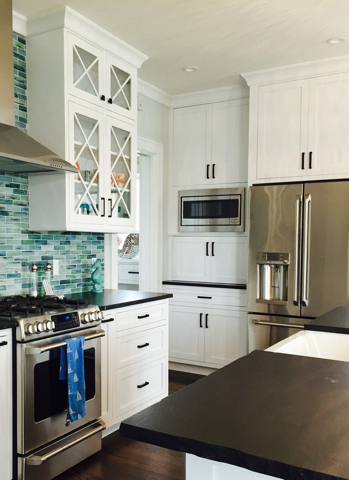 Photo of a mid-sized beach style u-shaped eat-in kitchen in New York with a farmhouse sink, shaker cabinets, white cabinets, granite benchtops, blue splashback, glass tile splashback, stainless steel appliances, medium hardwood floors and with island.
