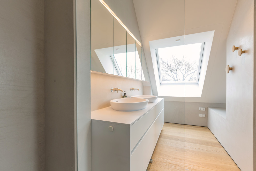 Large modern master bathroom in Munich with flat-panel cabinets, white cabinets, a drop-in tub, a wall-mount toilet, beige tile, travertine, white walls, light hardwood floors, a vessel sink, solid surface benchtops and beige floor.