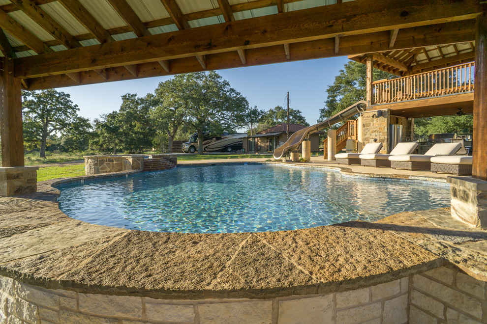 Photo of a large country backyard custom-shaped pool in Austin with a water slide and natural stone pavers.