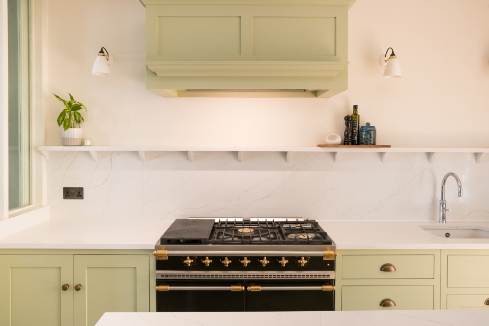Bild på ett stort funkis vit vitt kök, med en integrerad diskho, skåp i shakerstil, gröna skåp, bänkskiva i kvartsit, vitt stänkskydd, stänkskydd i sten, svarta vitvaror, ljust trägolv, en köksö och brunt golv