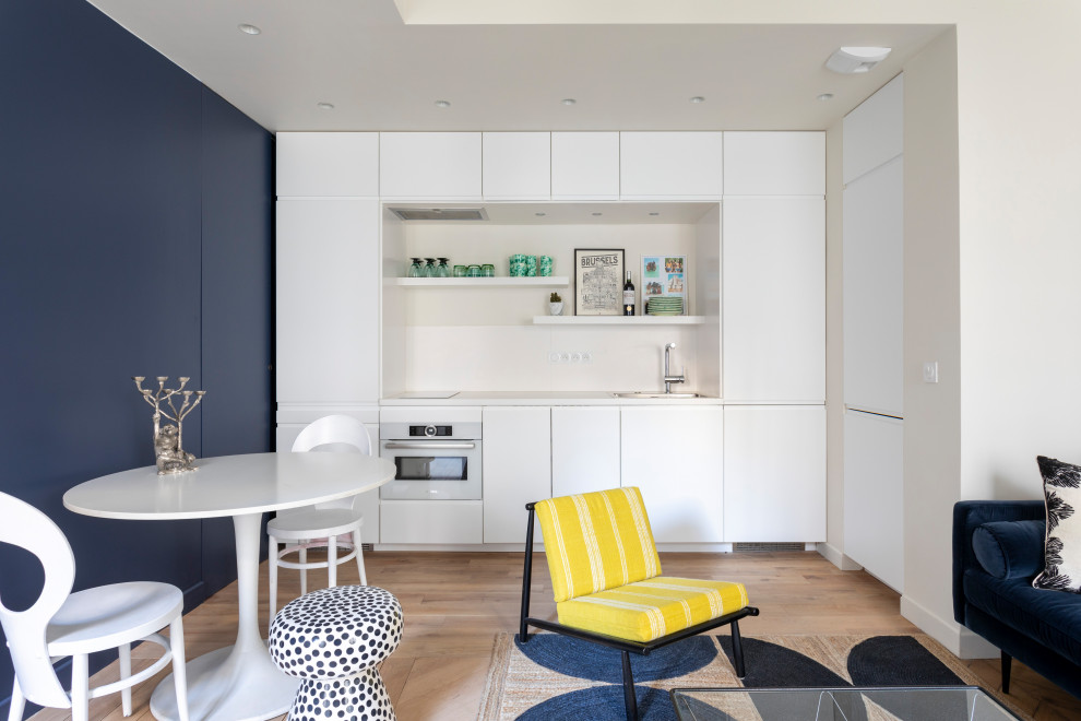 Small contemporary l-shaped open plan kitchen in Other with a single-bowl sink, beaded inset cabinets, white cabinets, laminate benchtops, white splashback, ceramic splashback, white appliances, medium hardwood floors, brown floor, white benchtop and recessed.