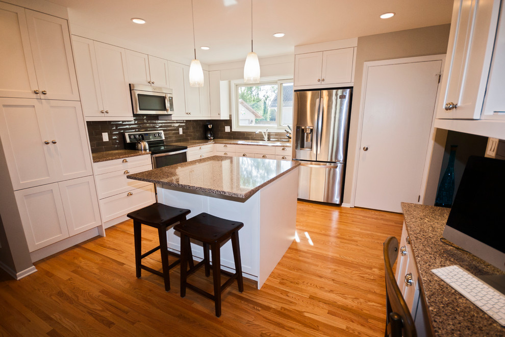 Mid-sized transitional l-shaped light wood floor eat-in kitchen photo with a double-bowl sink, shaker cabinets, white cabinets, quartz countertops, brown backsplash, ceramic backsplash, stainless steel appliances and an island
