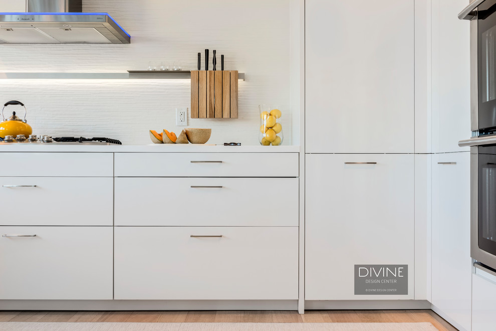Design ideas for a mid-sized contemporary u-shaped eat-in kitchen in Boston with an undermount sink, flat-panel cabinets, white cabinets, solid surface benchtops, white splashback, porcelain splashback, stainless steel appliances, light hardwood floors, a peninsula and beige floor.