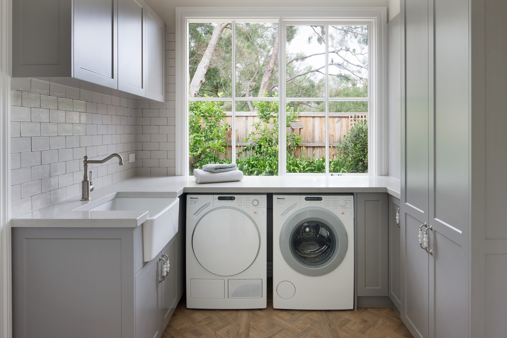 Mid-sized country u-shaped utility room in Melbourne with a farmhouse sink, beaded inset cabinets, beige cabinets, solid surface benchtops and a side-by-side washer and dryer.