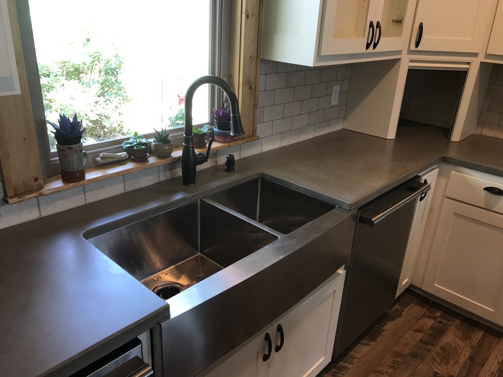 Mid-sized country l-shaped eat-in kitchen in Austin with a farmhouse sink, shaker cabinets, white cabinets, concrete benchtops, white splashback, stone tile splashback, stainless steel appliances, dark hardwood floors and brown floor.