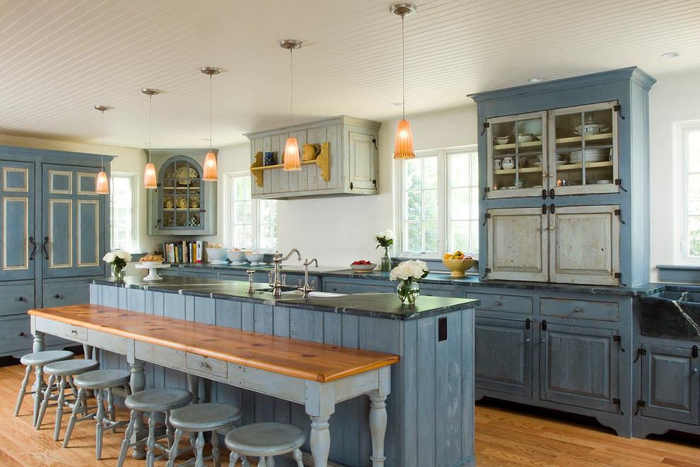 Photo of a traditional galley kitchen in Philadelphia with a farmhouse sink, raised-panel cabinets, blue cabinets, panelled appliances, medium hardwood floors, with island and brown floor.