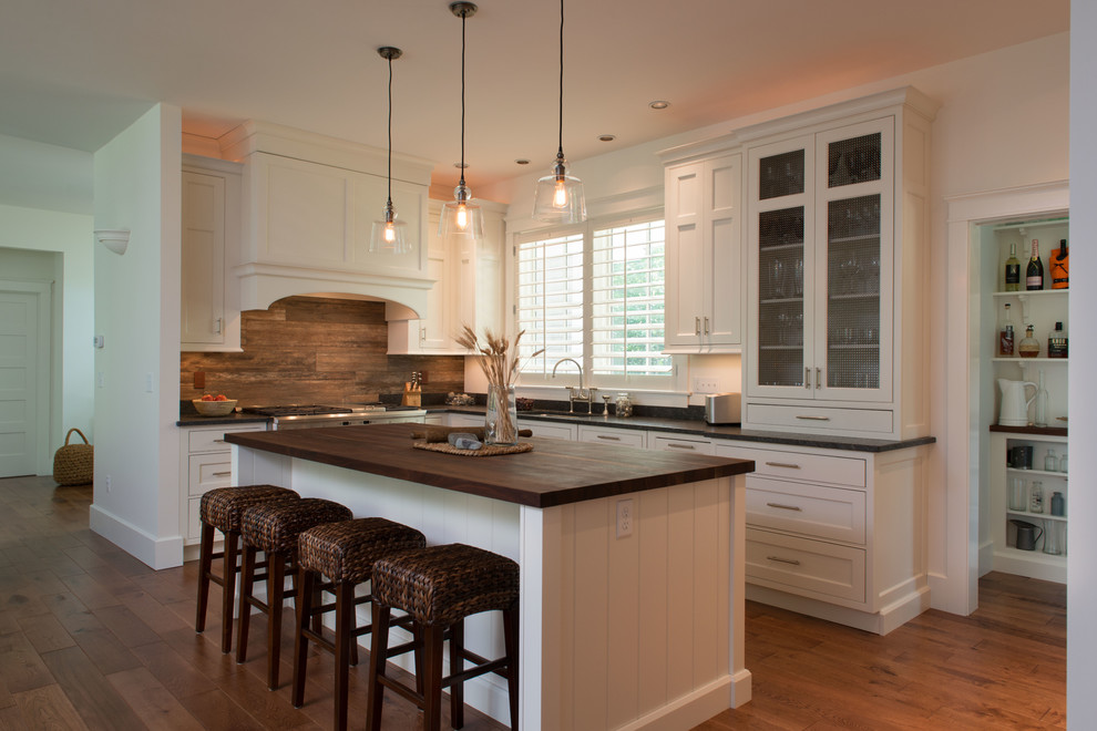 Mid-sized transitional l-shaped light wood floor eat-in kitchen photo in Boston with a single-bowl sink, recessed-panel cabinets, white cabinets, wood countertops, brown backsplash, ceramic backsplash, stainless steel appliances and an island
