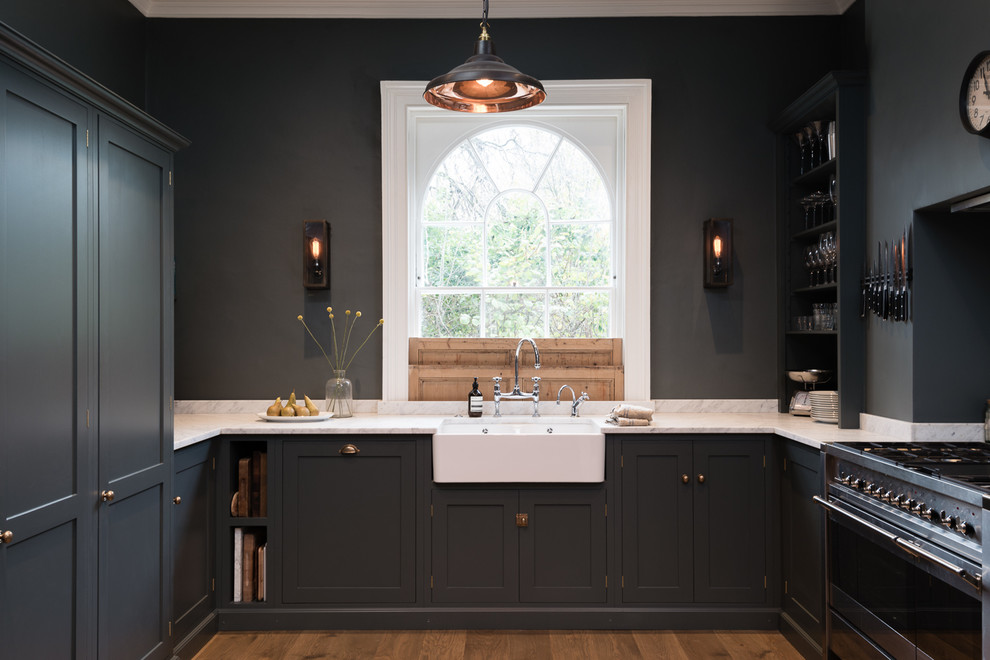 Photo of a transitional u-shaped kitchen in London with stainless steel appliances, a farmhouse sink, shaker cabinets, grey cabinets and dark hardwood floors.