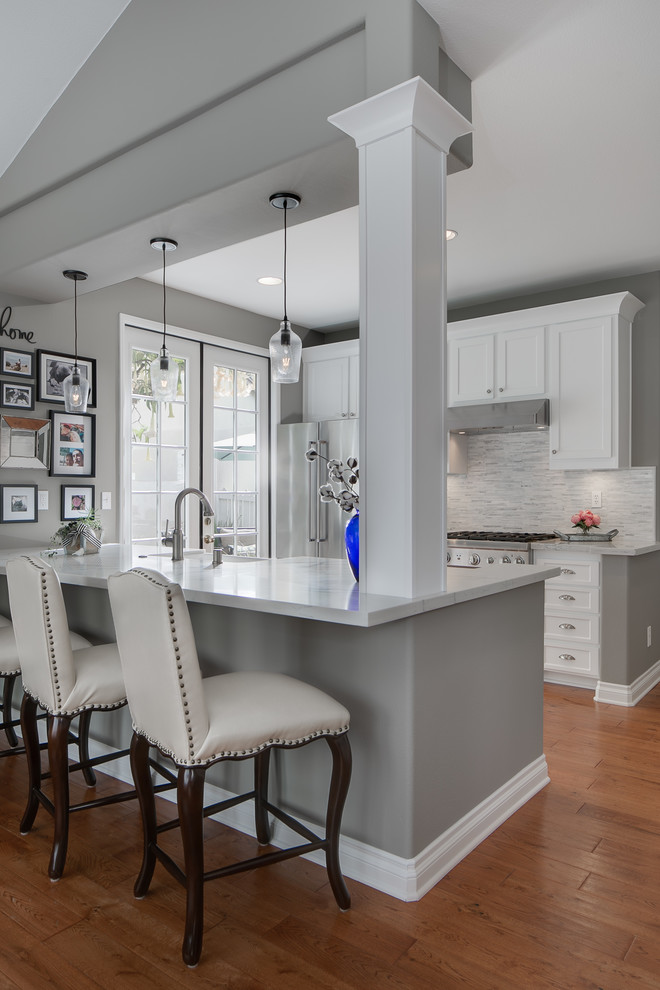 This is an example of a small contemporary galley kitchen in Orange County with a farmhouse sink, shaker cabinets, white cabinets, quartz benchtops, grey splashback, mosaic tile splashback, stainless steel appliances and with island.