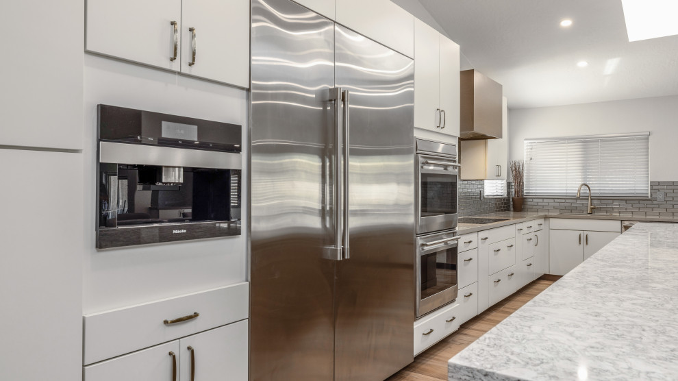 Design ideas for a large modern l-shaped eat-in kitchen in Phoenix with an undermount sink, flat-panel cabinets, white cabinets, quartz benchtops, grey splashback, glass tile splashback, stainless steel appliances, porcelain floors, with island, brown floor and grey benchtop.