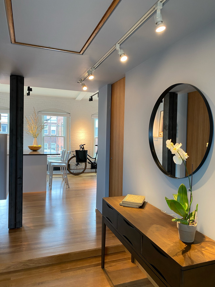 На фото: узкая прихожая среднего размера в современном стиле с синими стенами, паркетным полом среднего тона, одностворчатой входной дверью, белой входной дверью, балками на потолке и кирпичными стенами