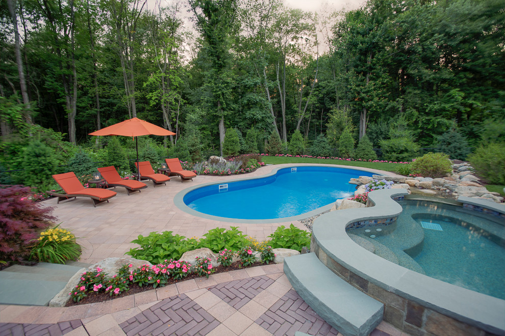 Photo of a large contemporary backyard kidney-shaped lap pool in New York with a hot tub and concrete pavers.