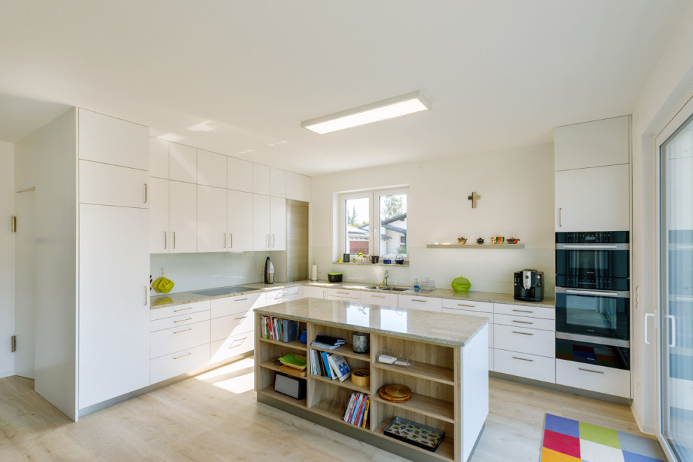 This is an example of a large contemporary l-shaped open plan kitchen in Stuttgart with a double-bowl sink, flat-panel cabinets, white cabinets, granite benchtops, white splashback, glass sheet splashback, black appliances, medium hardwood floors, with island, beige floor, grey benchtop and wallpaper.