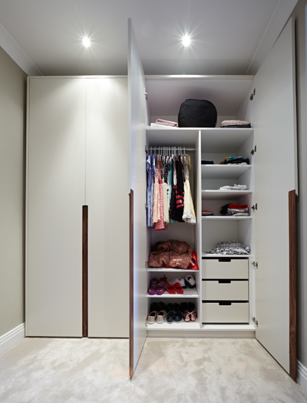 Mid-sized contemporary gender-neutral walk-in wardrobe in London with open cabinets, white cabinets and carpet.