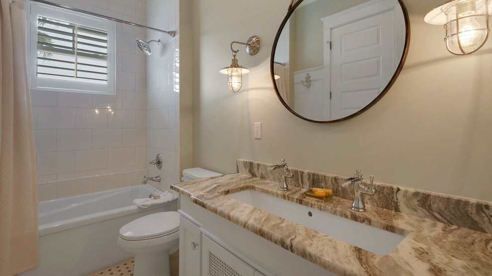 Inspiration for a mid-sized beach style 3/4 bathroom in Miami with recessed-panel cabinets, white cabinets, an alcove tub, a shower/bathtub combo, a two-piece toilet, beige tile, gray tile, stone slab, beige walls, ceramic floors, a trough sink and granite benchtops.