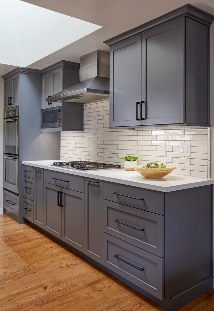 This is an example of a mid-sized transitional galley eat-in kitchen in San Francisco with a farmhouse sink, shaker cabinets, grey cabinets, quartzite benchtops, white splashback, subway tile splashback, stainless steel appliances, with island and white benchtop.