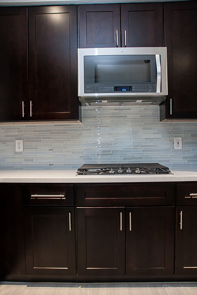 This is an example of a large modern l-shaped eat-in kitchen in Houston with shaker cabinets, dark wood cabinets, blue splashback, mosaic tile splashback, stainless steel appliances, with island, a double-bowl sink, quartz benchtops, porcelain floors, grey floor and white benchtop.