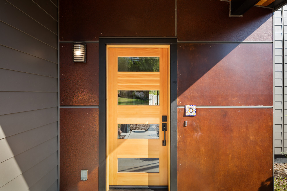 Inredning av en modern stor ingång och ytterdörr, med metallisk väggfärg, betonggolv, en enkeldörr, mellanmörk trädörr och grått golv