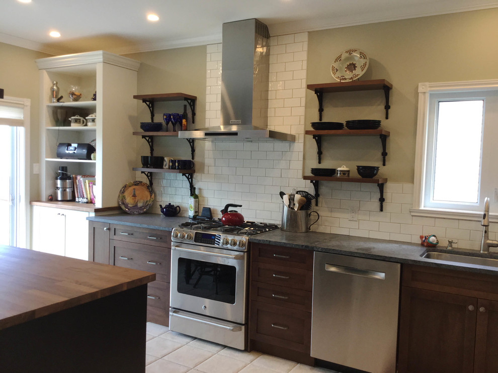 Inspiration for a mid-sized transitional l-shaped kitchen remodel in Ottawa with an undermount sink, shaker cabinets, dark wood cabinets, soapstone countertops, white backsplash, ceramic backsplash, stainless steel appliances and an island