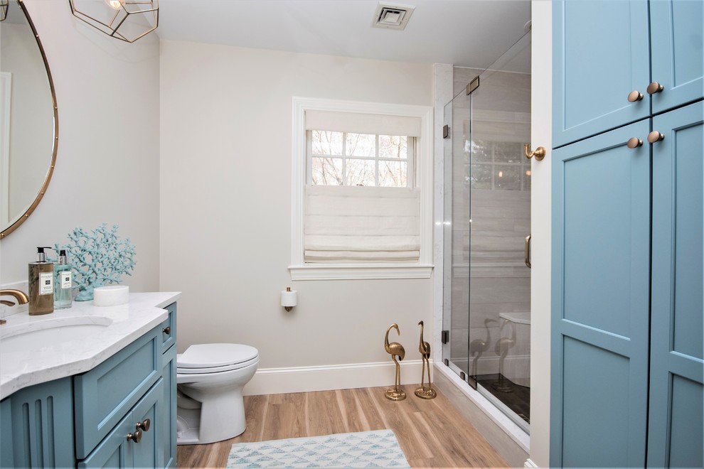 This is an example of a large transitional 3/4 bathroom in Providence with recessed-panel cabinets, blue cabinets, an alcove shower, a two-piece toilet, white tile, marble, white walls, vinyl floors, an undermount sink, marble benchtops, beige floor and a hinged shower door.