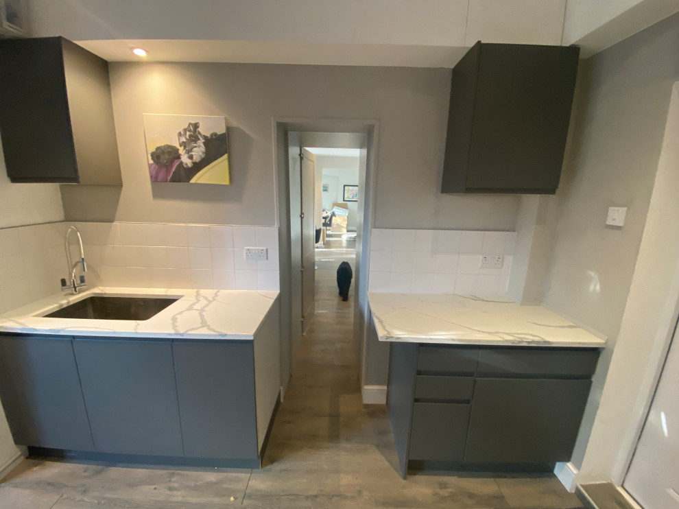 Large contemporary galley utility room in London with a drop-in sink, flat-panel cabinets, grey cabinets, quartzite benchtops, white splashback, porcelain splashback, beige walls, laminate floors, a side-by-side washer and dryer, grey floor and multi-coloured benchtop.