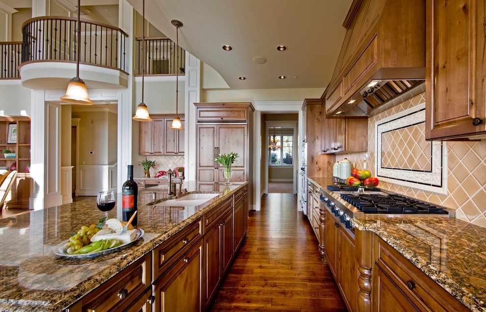 Inspiration for a traditional galley kitchen in Seattle with granite benchtops, raised-panel cabinets, medium wood cabinets, beige splashback, panelled appliances and brown floor.
