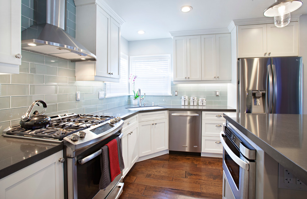 Inspiration for a mid-sized transitional l-shaped medium tone wood floor and brown floor open concept kitchen remodel in Orange County with an undermount sink, shaker cabinets, white cabinets, quartz countertops, green backsplash, glass tile backsplash, stainless steel appliances and an island