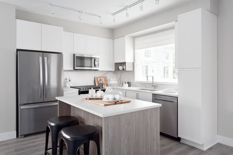 Example of a transitional l-shaped kitchen design in Vancouver with a double-bowl sink, shaker cabinets, white cabinets, white backsplash, marble backsplash, stainless steel appliances, an island and white countertops